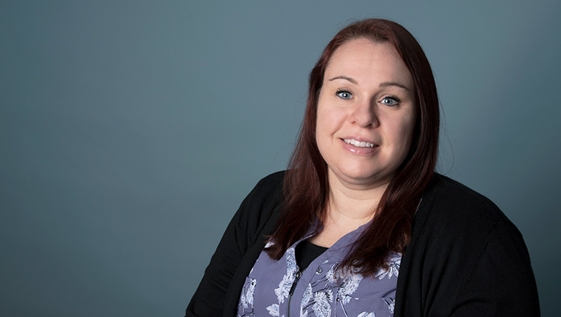 Female with dark hair smiling in front of studio lit gray backdrop
