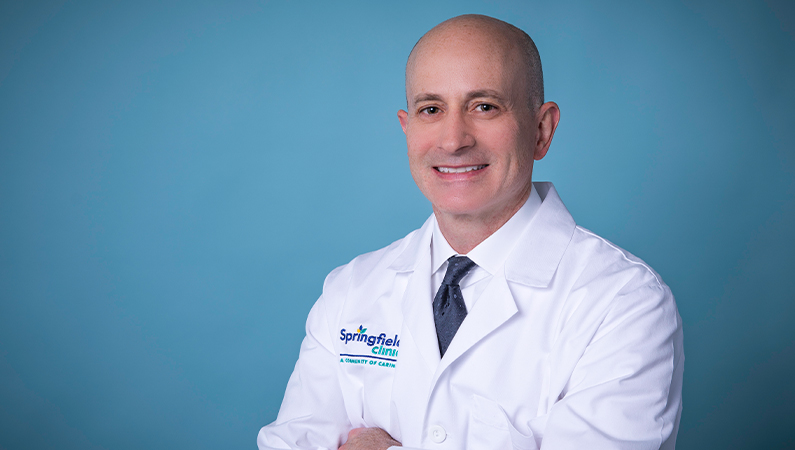 Male doctor wearing white coat smiling with arms crossed.