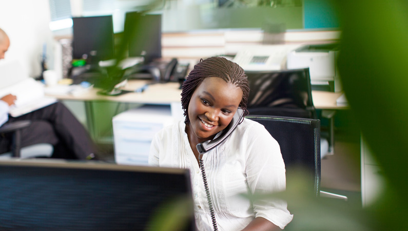Female in office desk setting smiling while talking on the phone.