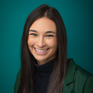 Female nurse practitioner smiling in front of teal blue backdrop.