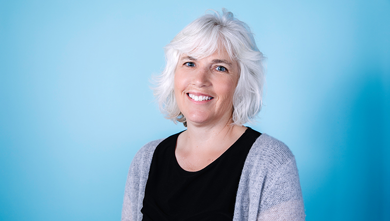 Female physical therapist smiling in front of a blue backdrop.