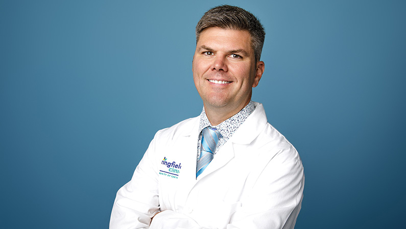 Male nurse practitioner wearing white medical coat smiling in professional headshot.