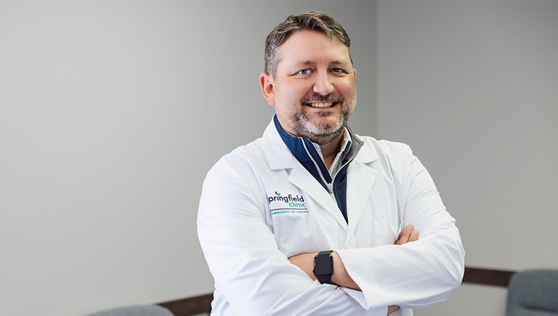 Male podiatrist wearing white medical coat smiling in medical office setting.