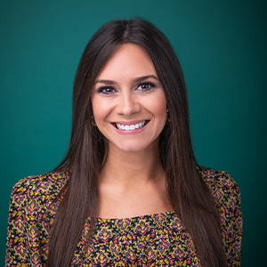 Female nurse practitioner smiling in front of a teal blue backdrop.