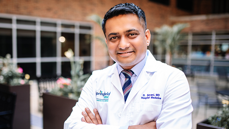 Male wearing white medical coat smiling in lobby setting