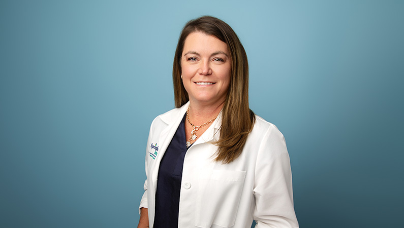 Female nurse wearing white medical coat smiling in front of blue photo background