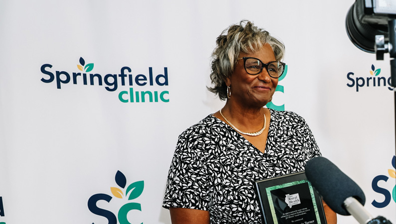 Senator Doris Turner smiling in front of a Springfield Clinic press conference backdrop.