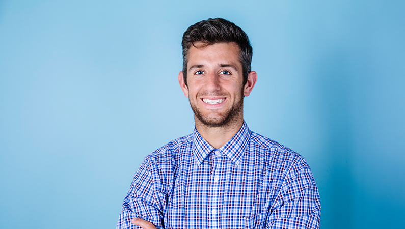 Male physical therapist smiling in front of a blue background.