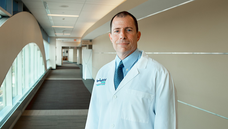 Male wearing white medical coat posing in well-lit hallway