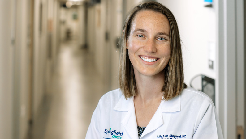 Female with short brown hair wearing white medical coat smiling in hallway