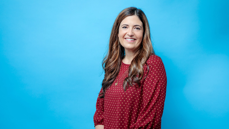 Female physician assistant smiling in front of a light blue backdrop.