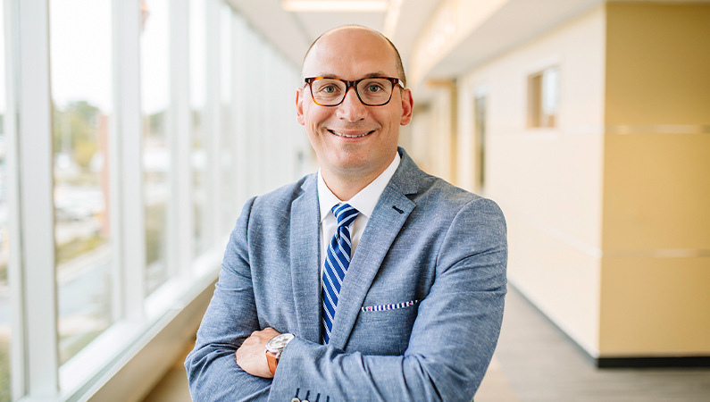 Male provider wearing glasses smiling in naturally lit hallway.