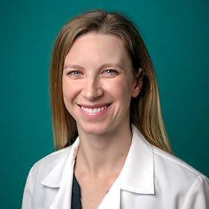 Female dermatology doctor smiling in front of a teal blue backdrop.