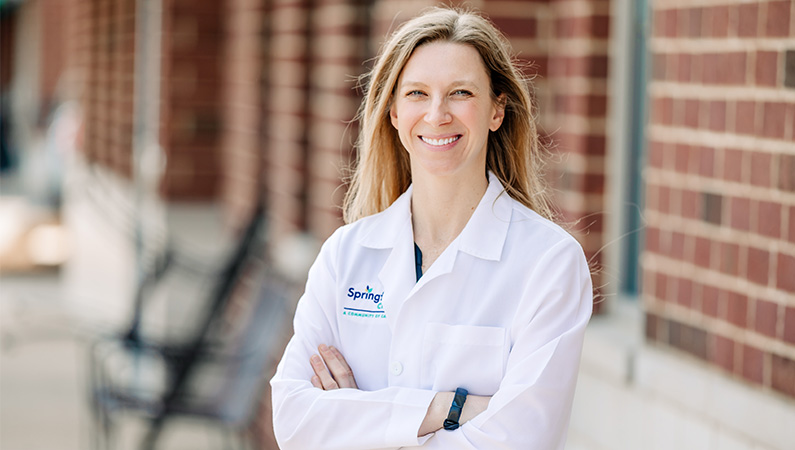 Female dermatology doctor in white coat smiling in an outdoor setting.