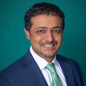 Male plastic surgery doctor smiling in front of teal blue backdrop.