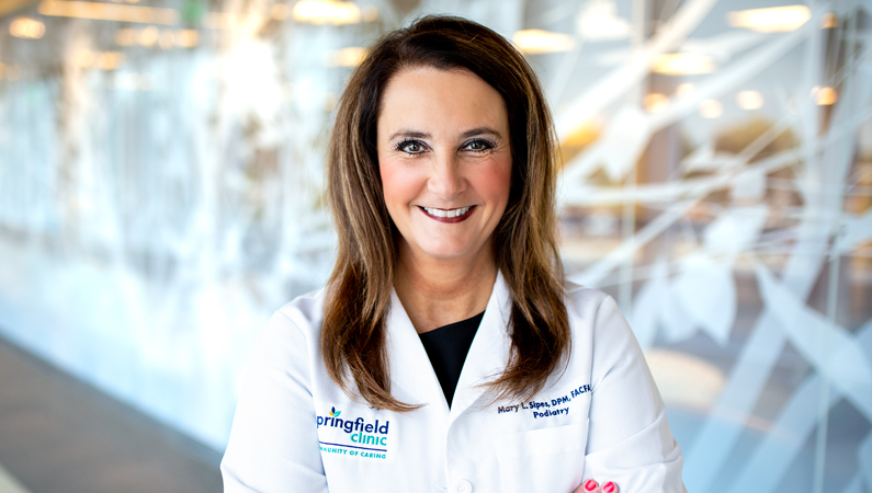 Female with dark hair wearing white medical coat smiling in front of wall mural