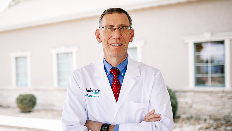 Male physician in white coat smiling in bright outdoor setting