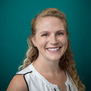 Female internal medicine doctor smiling in front of a teal blue backdrop.