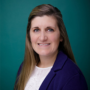 Female nurse practitioner smiling in front of teal photo backdrop.