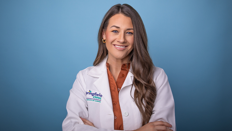 Female in white medical coat posing in front of light blue background