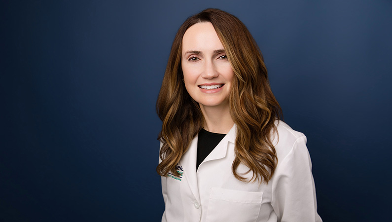 Female wearing while medical coat smiling in front of blue background