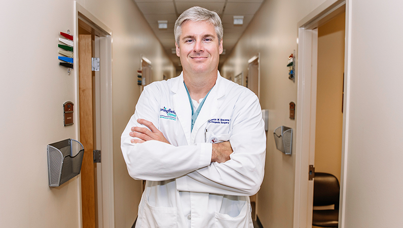 Male wearing white medical coat posing in medical office hallway