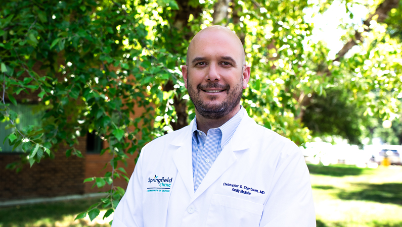 Male wearing white medical coat smiling in outdoor setting