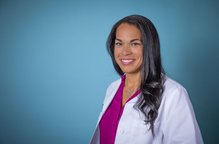 Female in white coat smiling in front of a blue backdrop.