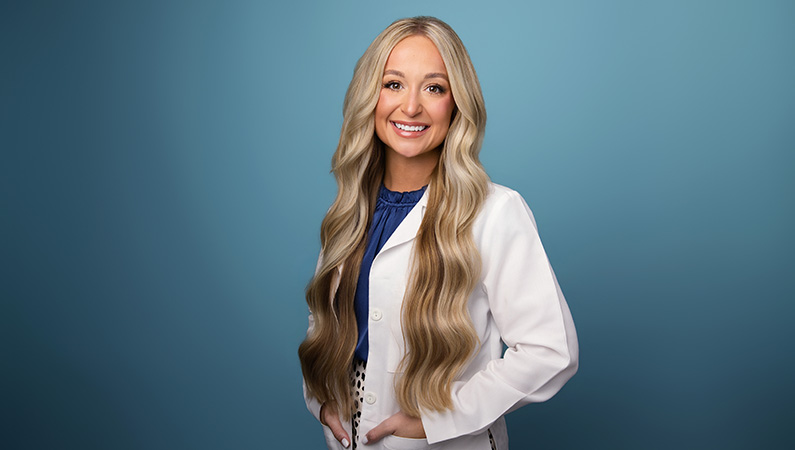 Female nurse practitioner wearing white medical coat smiling in professional headshot