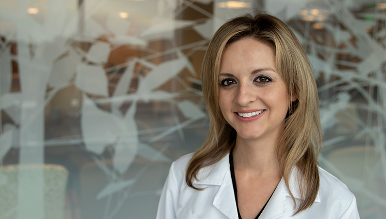 Woman smiling in front of a clear wall with a white tree decal.