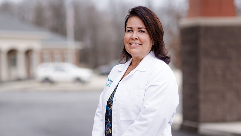 Female provider in white medical coat smiling in outdoor setting.