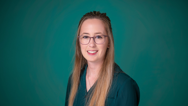 Female athletic trainer smiling in front of a teal blue backdrop.