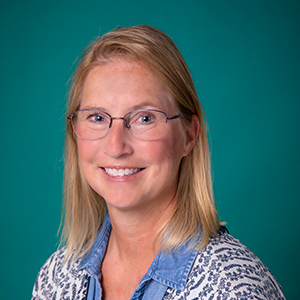 Female nurse practitioner professional headshot in front of a teal blue backdrop.
