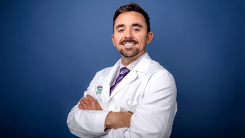 Male doctor in a white medical coat smiling in front of blue backdrop.