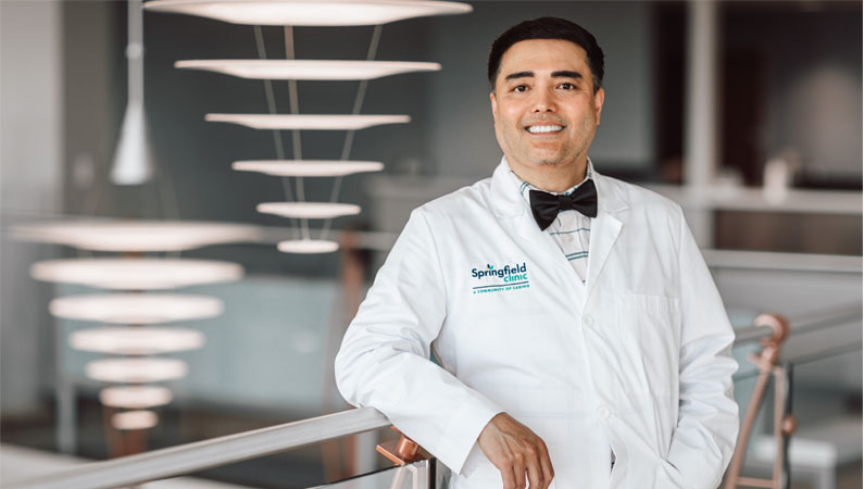 Male neurology doctor in white coat smiling in naturally lit doctor's office.