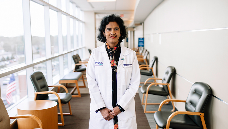 Female internal medicine doctor in white coat smiling in a patient waiting room.