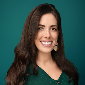 Female nurse with long brown hair smiling in front of green photo backdrop.