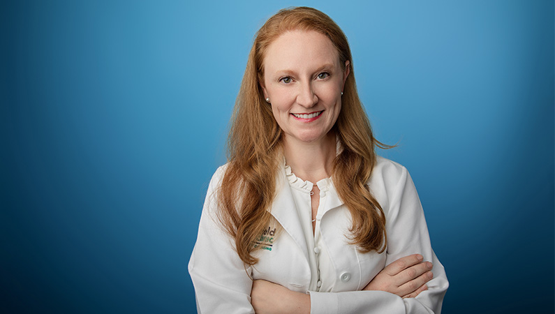 Female physician assistant wearing white medical coat smiling with arms crossed.