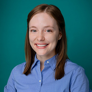 Female in blue shirt smiling in front of blue photo backdrop.
