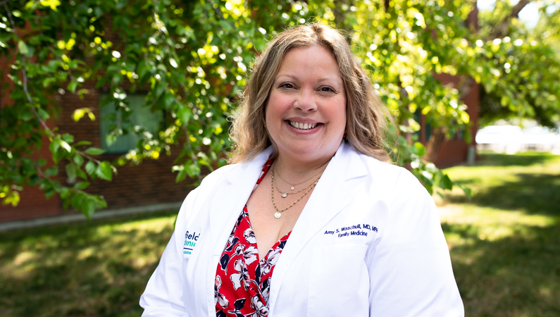 Female wearing white medical coat smiling in outdoor setting