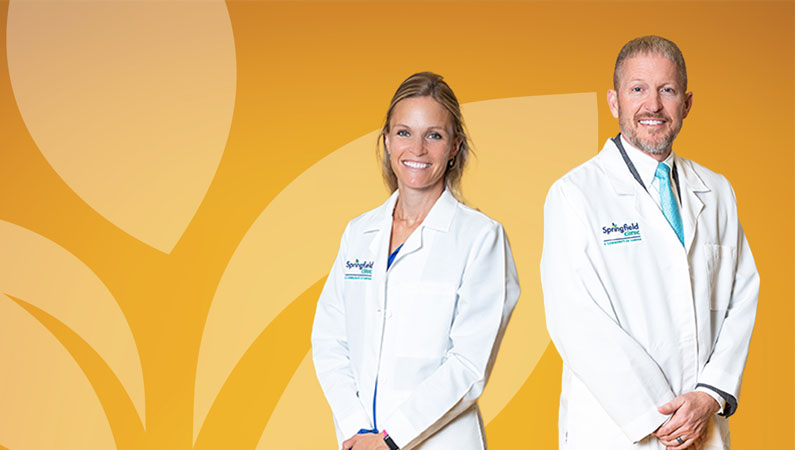 Two pediatric doctors in white coats smiling in front of yellow photo backdrop.