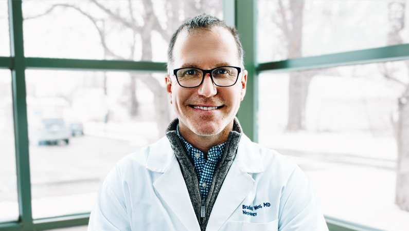 Man wearing glasses smiling in front of a window.