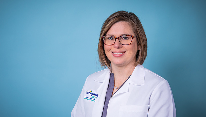 Nurse practitioner smiling in a white coat in front of a blue backdrop.
