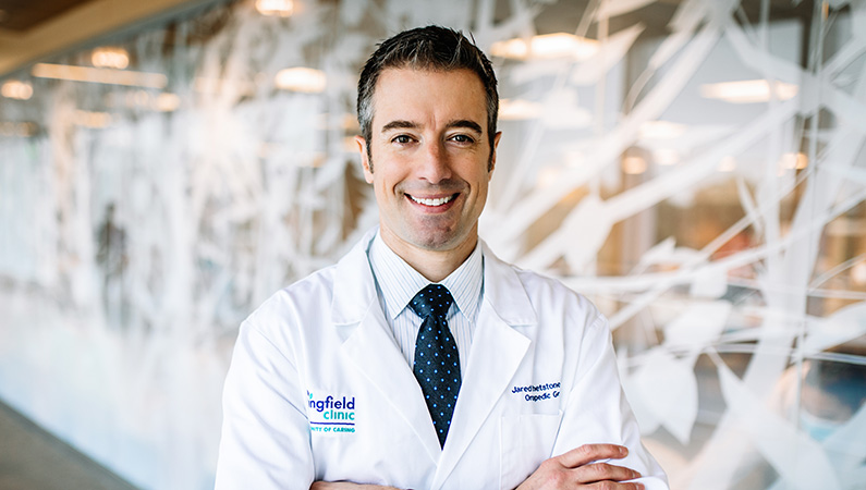 Male smiling with his arms crossed wearing a white medical coat