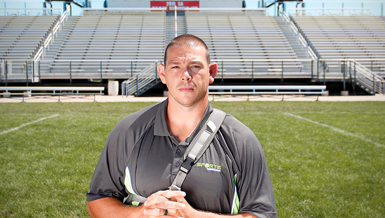 Male with short dark hair posing in workout gear in front of football field