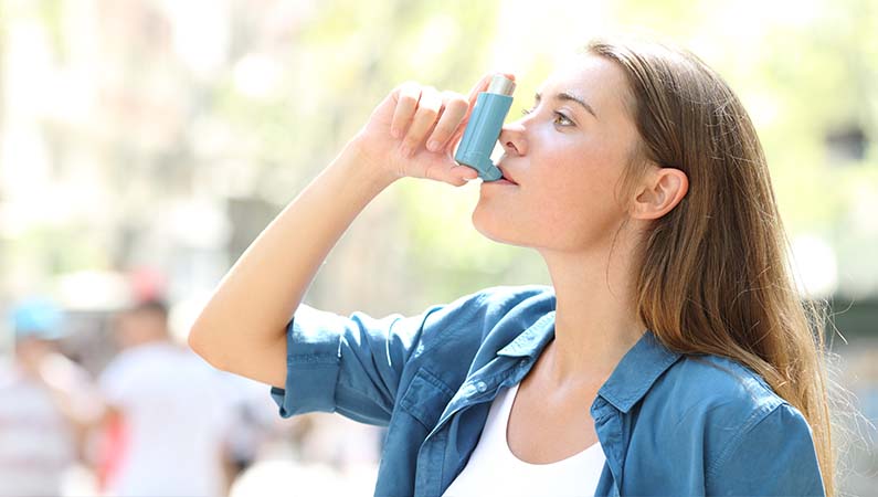 Woman using inhaler outside.