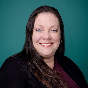 Female doctor smiling in front of blue photo backdrop.