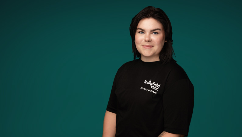 Female athletic trainer smiling in front of teal green photo backdrop.