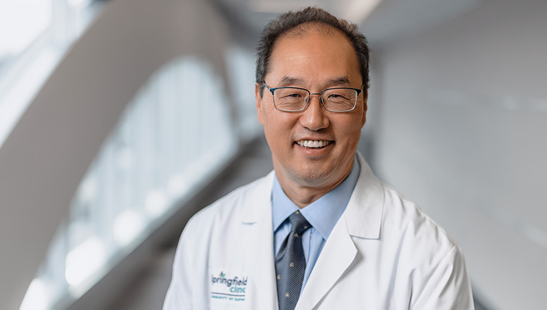 Male cardiologist wearing white medical coat smiling.