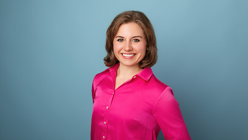 Female wearing pink button down shirt smiling in front of blue background